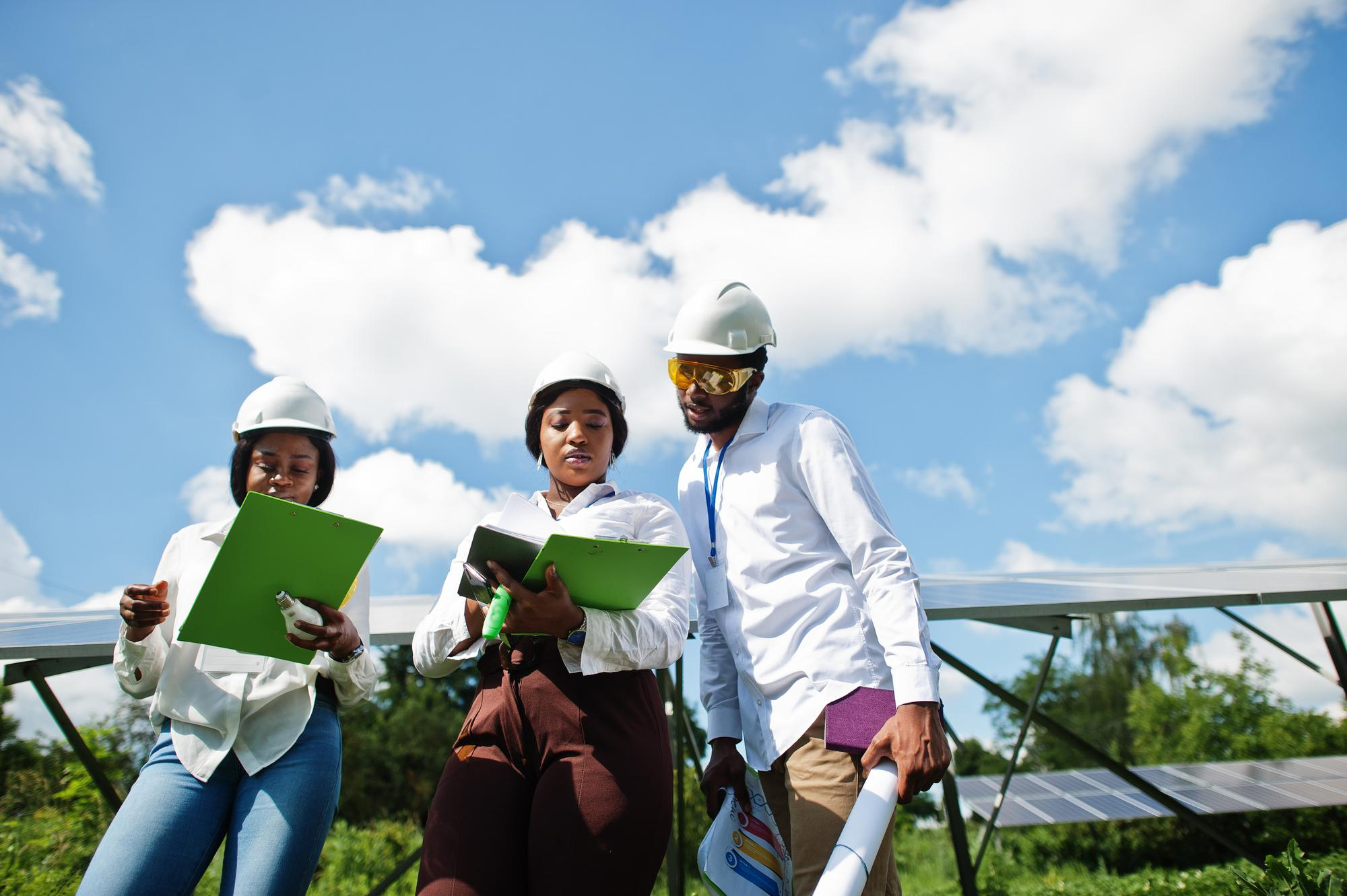 Young African energy professionals reviewing plans beside solar panels